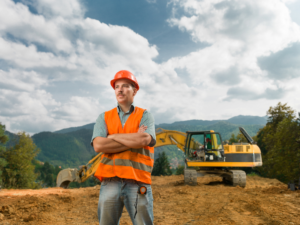 front view of engineer standing on construction site outdoors with excavator in background